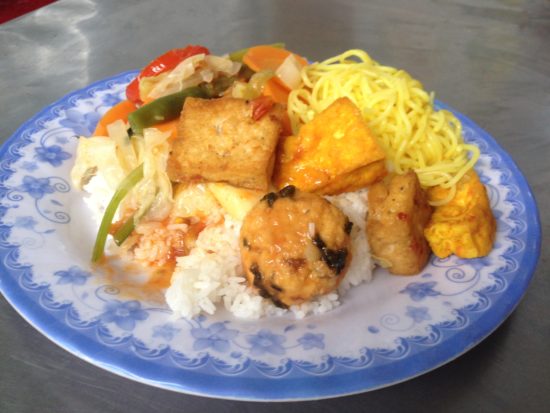 Photo contains a plate of rice with various vegetables, tofu, and noodles placed on top.