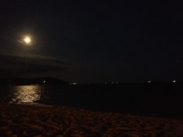 Night photo with the full moon to the left and its reflection in the ocean below.