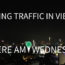 Photo of a city skyline at night with white text in the foreground that says "Dodging Traffic in Vietnam. Where Am I Wednesday"