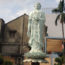 Photo of a large, light green Buddha standing on a lotus flower surrounded by palm trees.