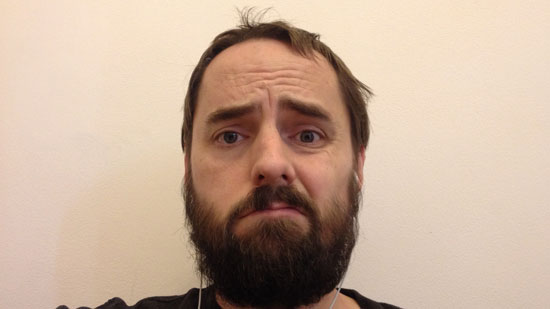 Picture of a sad white man with a beard against a wall.