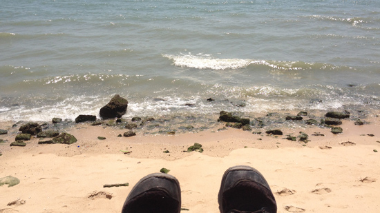 Photo of a rocky beach with white waves and a pair of shoes in the foreground.