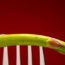 Image contains a dark red background with a silver fork coming up from the bottom of the frame. On the fork, a single piece of asparagus is visible. However, the image is cropped so that neither the tip or the bottom of the asparagus is visible.
